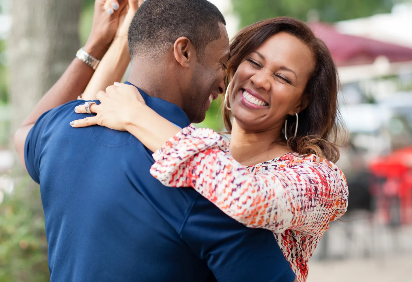 An African American couple is outside hugging and dancing with one another.