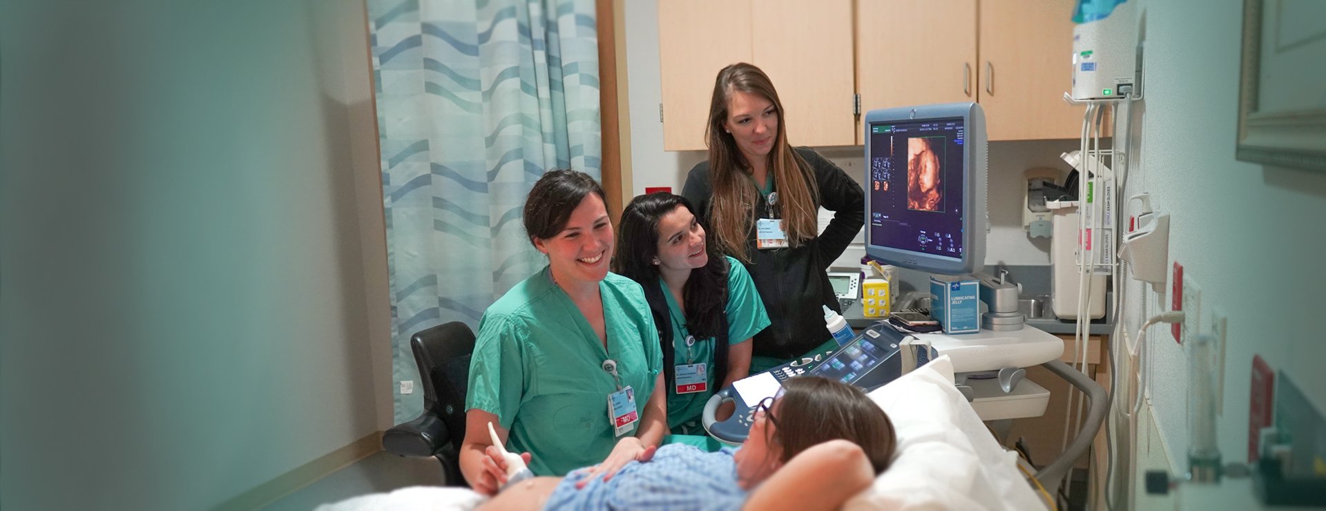 2 OBYGN residents smile with a patient as they conduct her ultrasound showing her growing baby