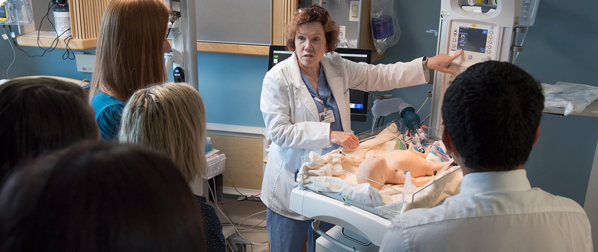 A residency instructor shows residents something on a monitor attached to a medical baby model